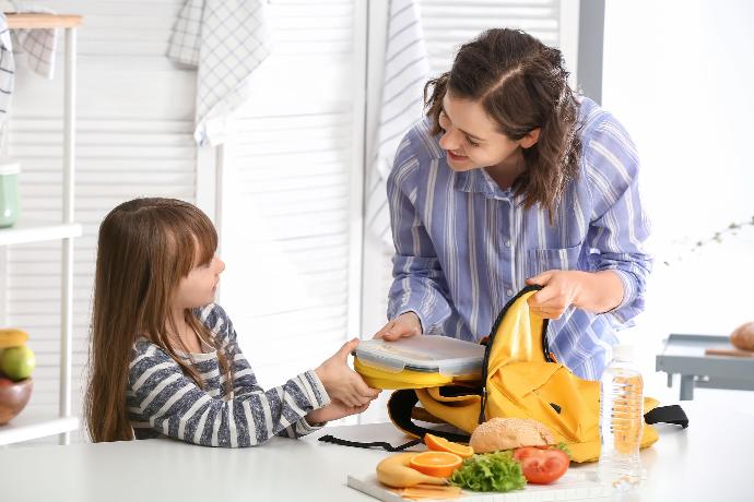Un maman prépare le sac de sa fille pour l'école avec sa lunch box