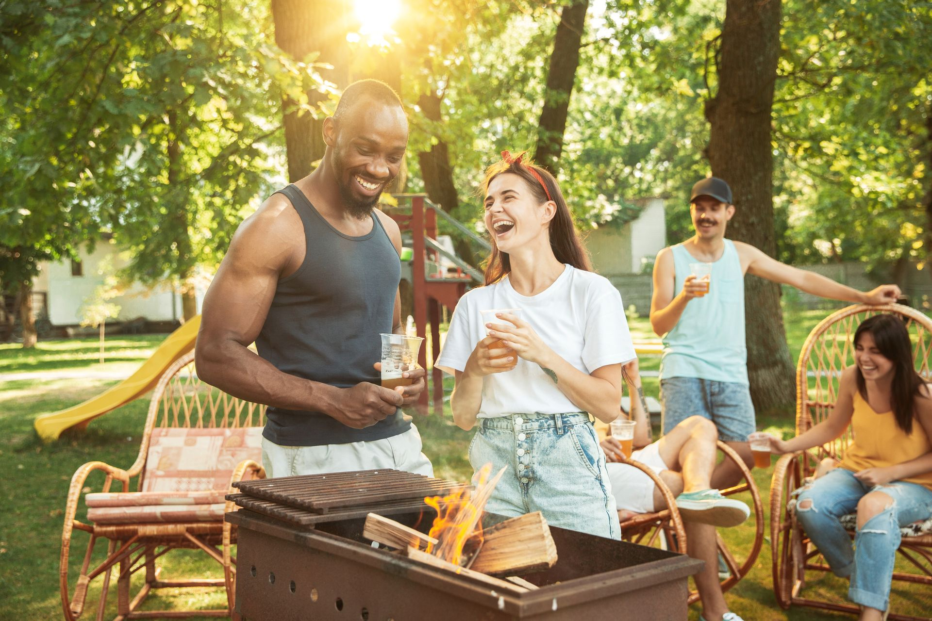 Jeune femme et jeune homme riant devant un barbecue, un verre de bière à la main 